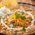 Bowl of creamy white chicken chili with cream cheese, topped with cilantro and tortilla strips