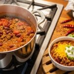 Bowl of Easy Stovetop Ground Beef Chili Recipe topped with shredded cheese, sour cream, and green onions — hearty homemade chili recipe on the table.